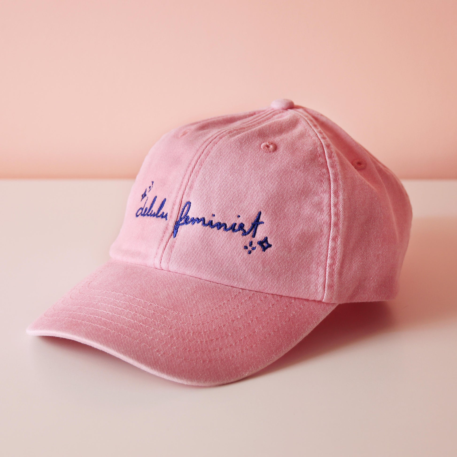 seitliche Ansicht einer rosa Cap mit dem aufgestickten Schriftzug "Delulu Feminist" in blau 