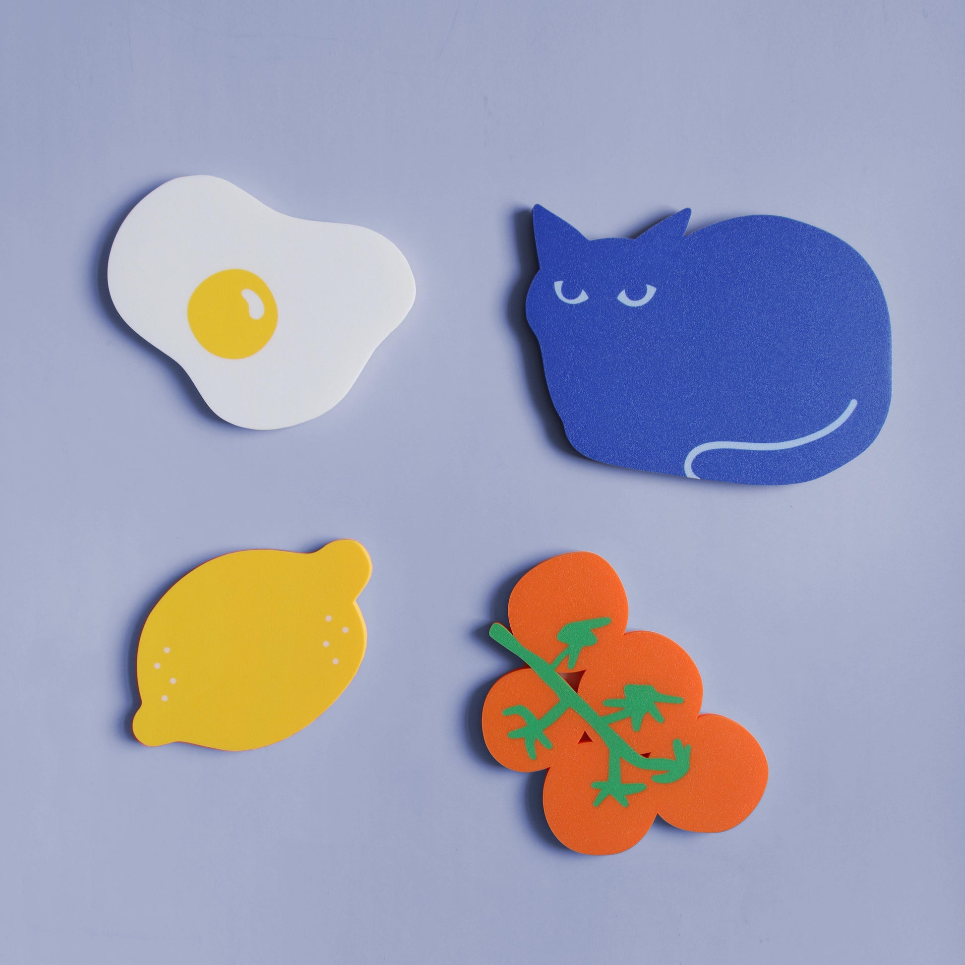 overview of different colorful wall decor designs such as a fried egg, a blue cat, a lemon and a bunch of tomatoes on a light blue background